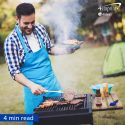 Smiling man wearing blue apron flipping burgers on an outdoor grill.