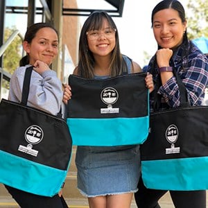 Three women posing for the camera holding their black and teal swag bags