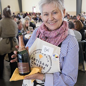 A volunteer smiling for the camera wearing a branded apron and holding a wine bottle