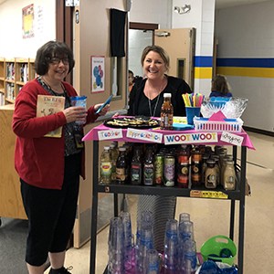 Staff standing next to cart full of drinks, cups and snacks