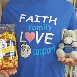 A woman in a blue shirt holds a bag of popcorn and a stuffed elephant with logo. 