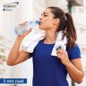 Woman with towel around her neck taking a drink of water.