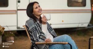 Woman sitting outdoors in a chair. She is wrapped in a plaid blanket and drinking coffee.