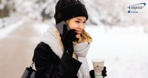 Smiling woman outside in cold-weather holding coffee and talking on phone.