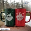 Two mugs imprinted with a logo in an outdoor winter scene.