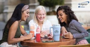Three women talking at a table. They each have a piece of branded drinkware.