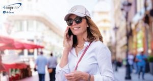 Person wearing a cap and sunglasses while walking in a city and speaking on her mobile phone.