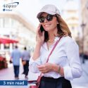 Person wearing a cap and sunglasses while walking in a city and speaking on her mobile phone.