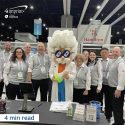Group of people and a scientist mascot at a trade show booth.
