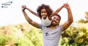 Child flying on father’s shoulders in outdoor summer setting.