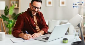 Smiling man writing in notebook. A wireless speaker is on his desk.