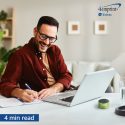 Smiling man writing in notebook. A wireless speaker is on his desk.