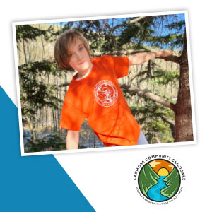 A child wearing a brightly colored orange shirt is hanging on a tree.