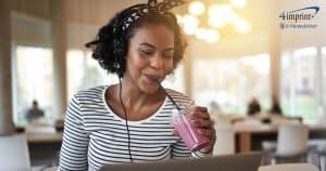 A young woman on her laptop and wearing headphones smiles as she sips a berry smoothie.