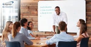 Man standing in front of whiteboard addressing a table of colleagues.