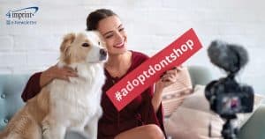 Female vlogger sitting on couch with dog holding a sign that says #adoptdontshop.