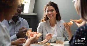 Woman sitting at breakroom table having pizza with co-workers.