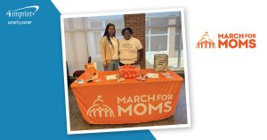 Two people standing behind branded event table.