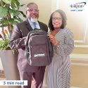 Man and woman holding a backpack with a logo.