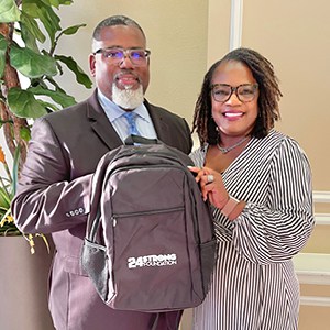 Man and woman holding a backpack with a logo.