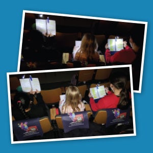Children using clip-on book lights to read their lines in a dark theatre.