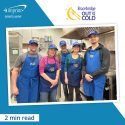 Group of cooks wearing branded hats and aprons in an industrial kitchen.