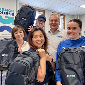 Smiling group of people carrying branded backpacks.