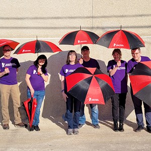 Group of people wearing matching T-shirts holding black and red umbrellas.