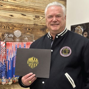 Smiling man holding a certificate holder with a logo.