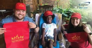 A man and woman wearing red baseball caps. A child with special needs in a matching hat sits between them.