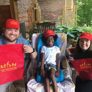 A man and woman wearing red baseball caps. A child with special needs in a matching hat sits between them.