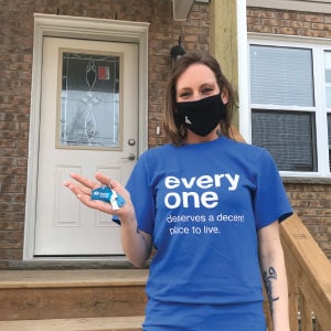 Woman on front steps of house holding Habitat for Humanity keychain.
