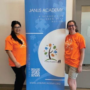 Two women wearing logoed T-shirts standing next to a banner.