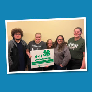 Group of smiling youth holding a 4-H sign.