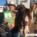 Woman standing next to a horse. She is holding a folder with a logo’d sticker.
