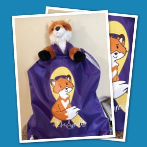 Fox stuffed animal peeking out of purple drawstring bag imprinted with a fox.