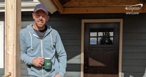Man standing on front porch next to dog. Man is holding a green branded coffee mug.