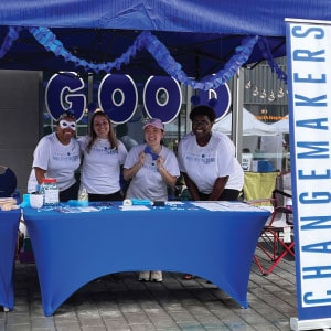 Four volunteers wearing branded white T-shirts smile at blue booth.