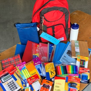 A backpack, water bottle and school supplies on a table.