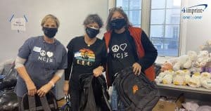 Three women wearing face masks with a logo and holding branded backpacks.