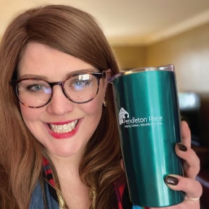 Woman wearing glasses is holding a turquoise metallic tumbler imprinted with a logo.
