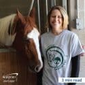 Woman wearing a branded T-shirt standing next to a horse.