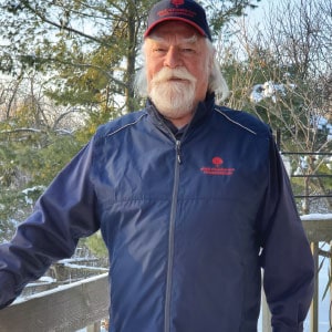 Man outside wearing a branded wind breaker and baseball cap.