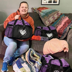 Woman sitting on sofa holding up branded duffel bag.