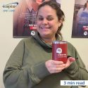 Woman holding red insulated mug with a logo. There are United Way posters on the wall behind her.