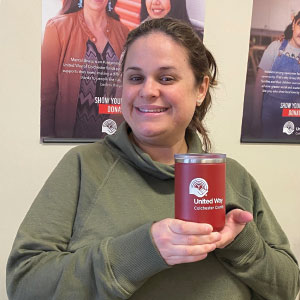Woman holding red insulated mug with a logo. There are United Way posters on the wall behind her.