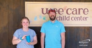 Man and woman standing by a childcare center. The woman holds a mug.