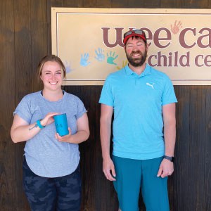 Man and woman standing by a childcare center. The woman holds a mug.
