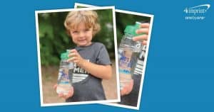 Smiling young boy holds clear branded water bottle with green lid.