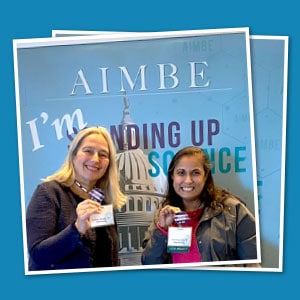 Two people holding up promotional buttons in front of a branded backdrop.